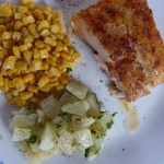 Cooked corvina on a plate with potatoes and corn.