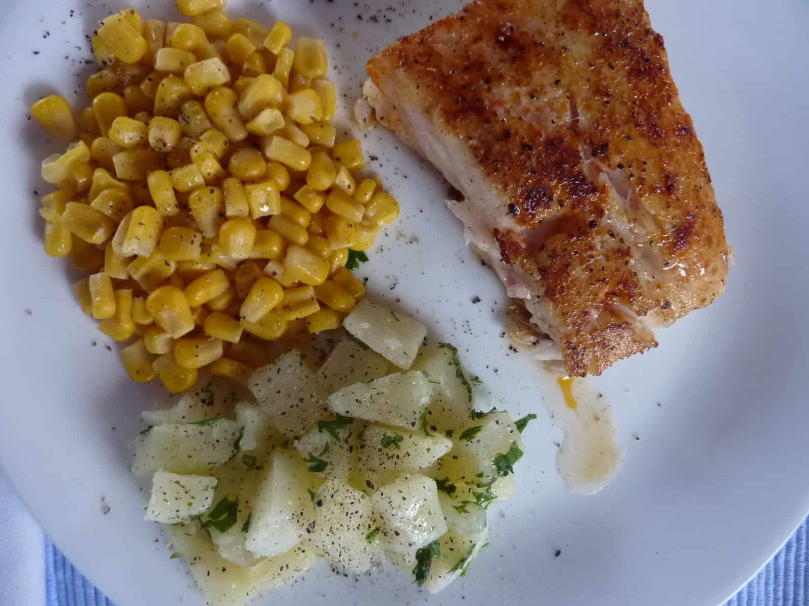 Cooked corvina on a plate with potatoes and corn.