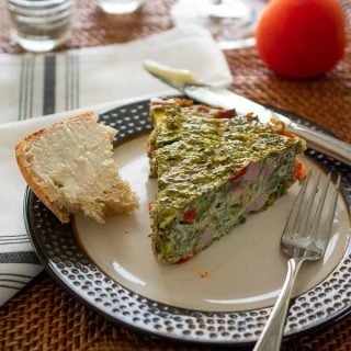 Plate with a slice of vegetable quiche and buttered bread.