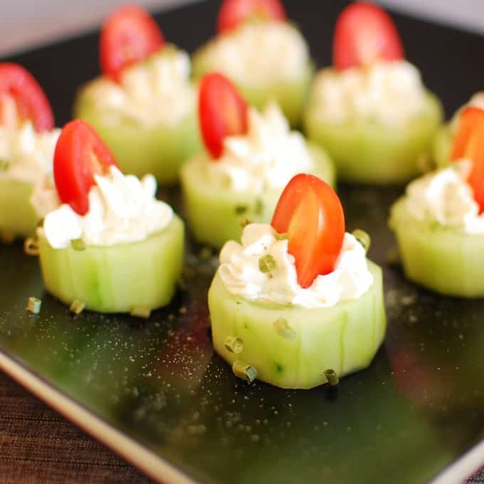 cucumber slices with piped on cream cheese and a halved grape tomato