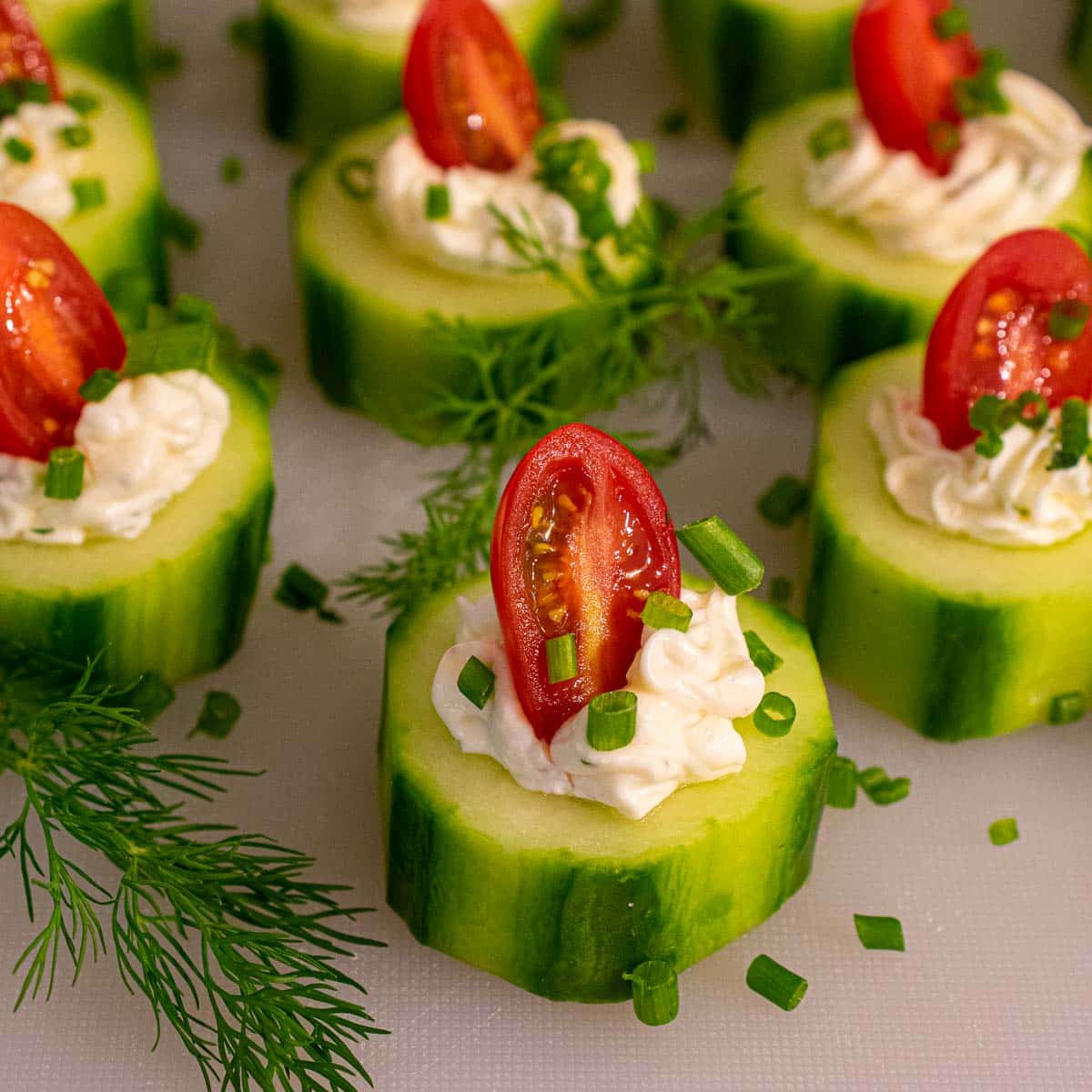 Cucumber appetizers with grape tomato halves and chive garnish.