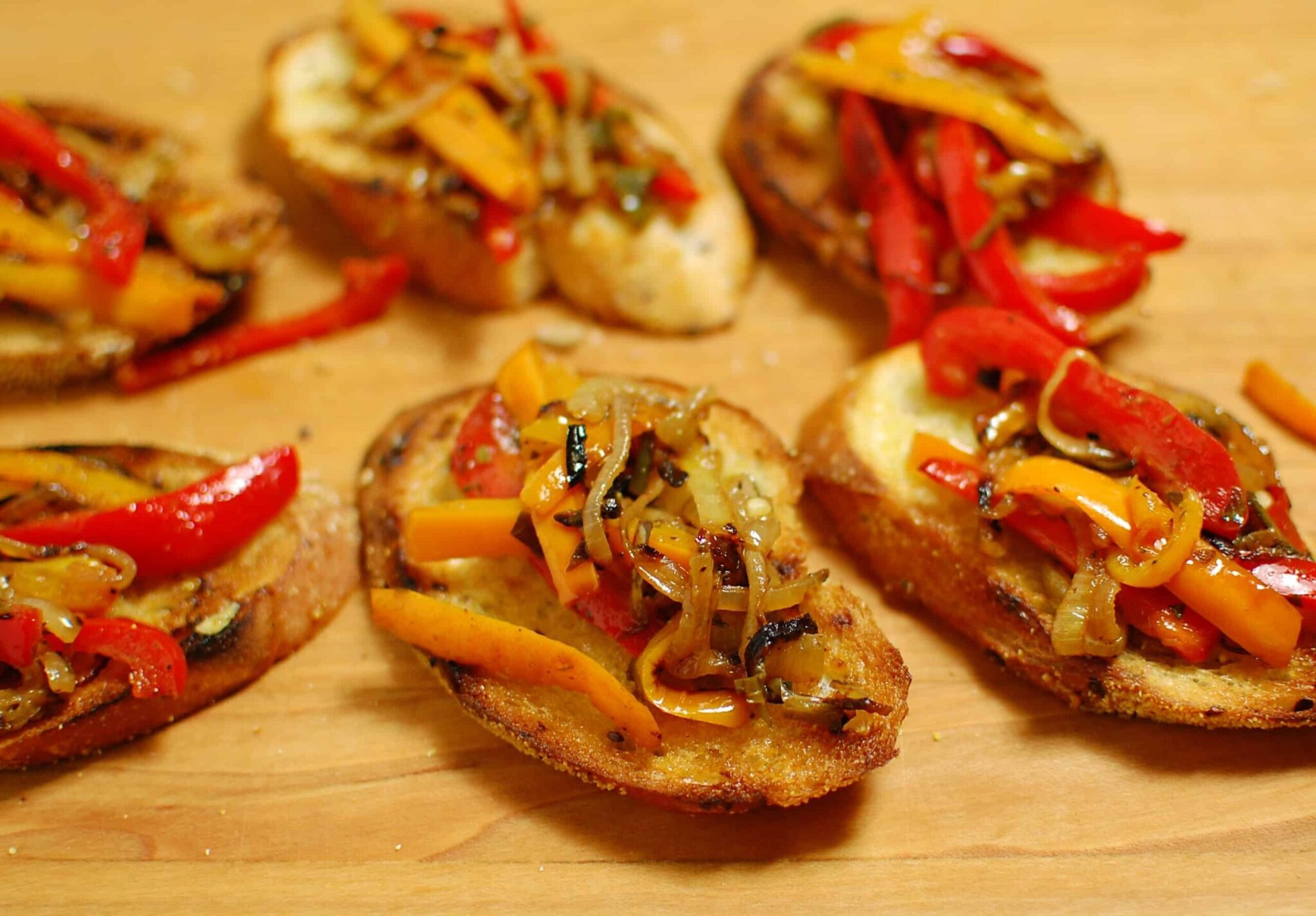 Bruschettas with peppers and onion on a cutting board.