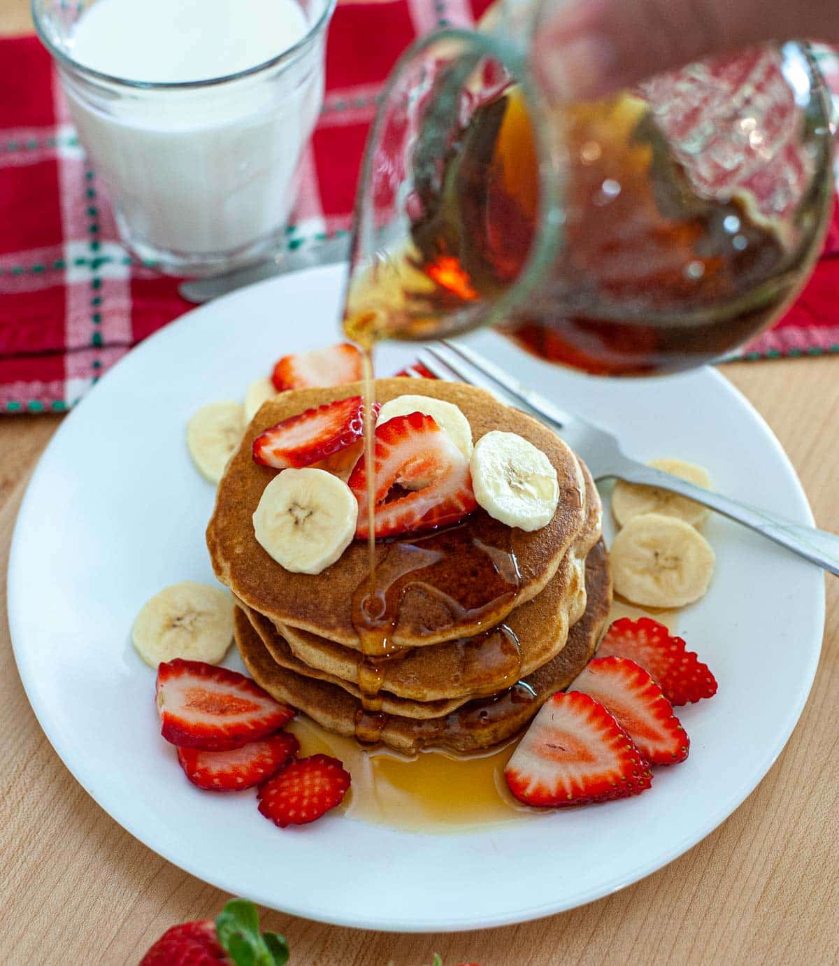 Stack of pancakes on a plate with strawberries and banana slices.