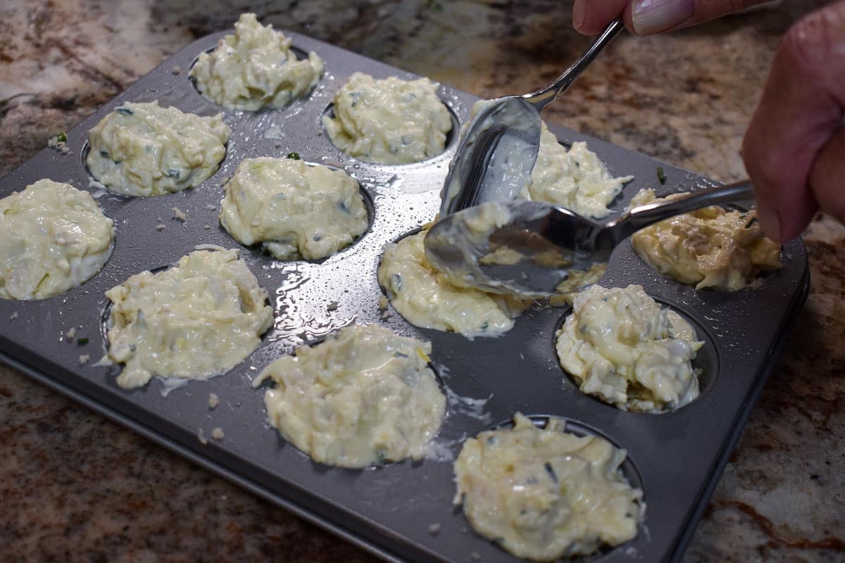 Crab cake batter being put into a mini muffin pan.