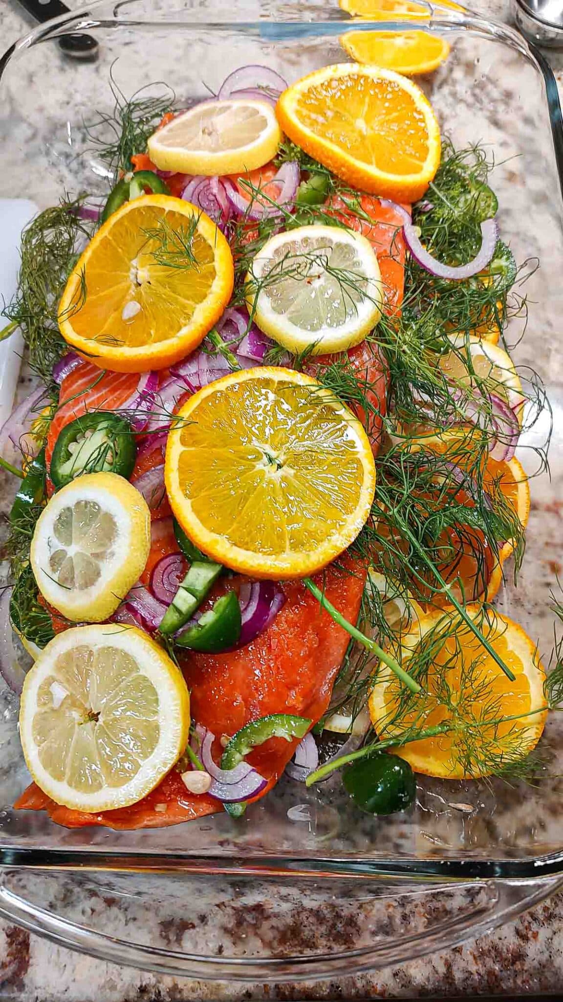 Salmon in a baking dish with orange and lemon slices with fresh dill weed.