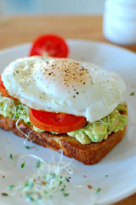 Close-up view of fried egg and tomato slice on Avocado toast.