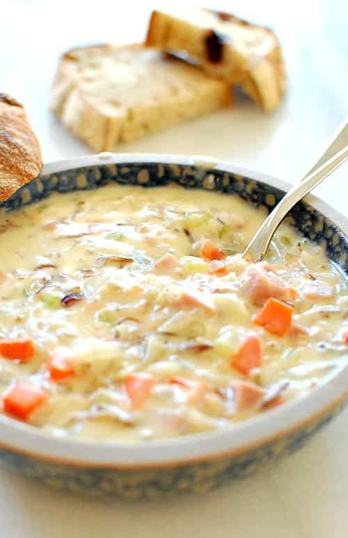 Ham wild rice soup in abowl with crusty bread in the background.