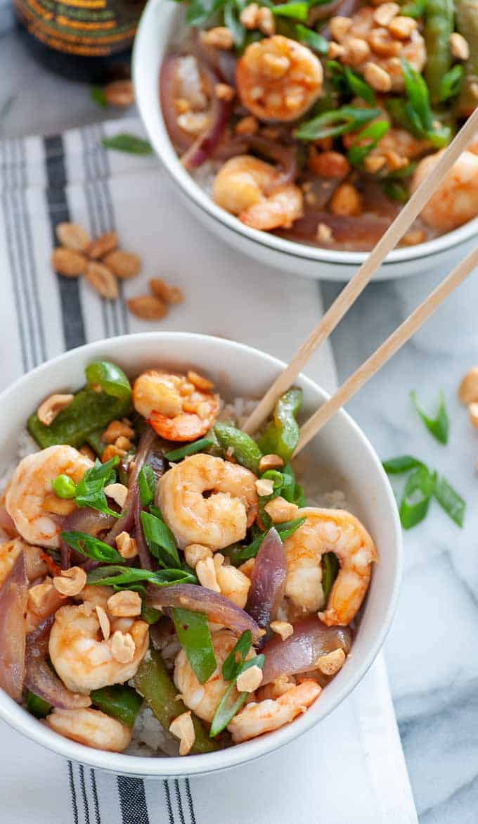 Bowls of spicy shrimp stir fry with peanuts and chop sticks.