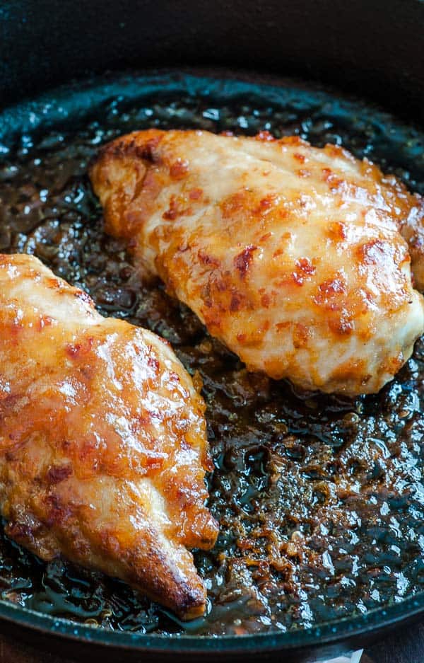 2 chicken breasts cooking in a skillet.