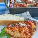 Side view if lasagna on a plate with the lasagna casserole in the background.