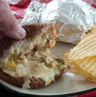 A cheesy sandwich on a plate with potato chips.