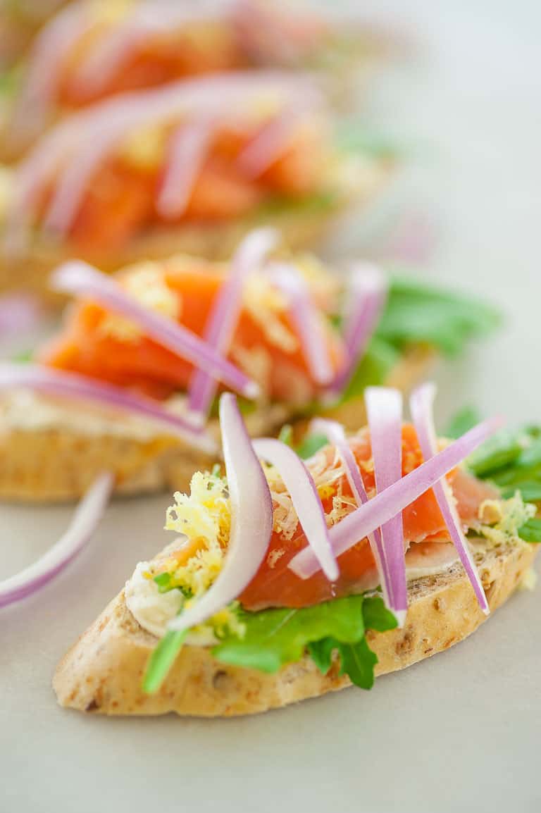 This is a smoked salmon appetizer with flavored cream cheese, arugula, lemon zest, and topped with sliced red onion. Only 82 calories for each. | joeshealthymeals.com