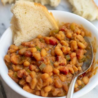 A bowl of stovetop baked beans with spoon and bread.