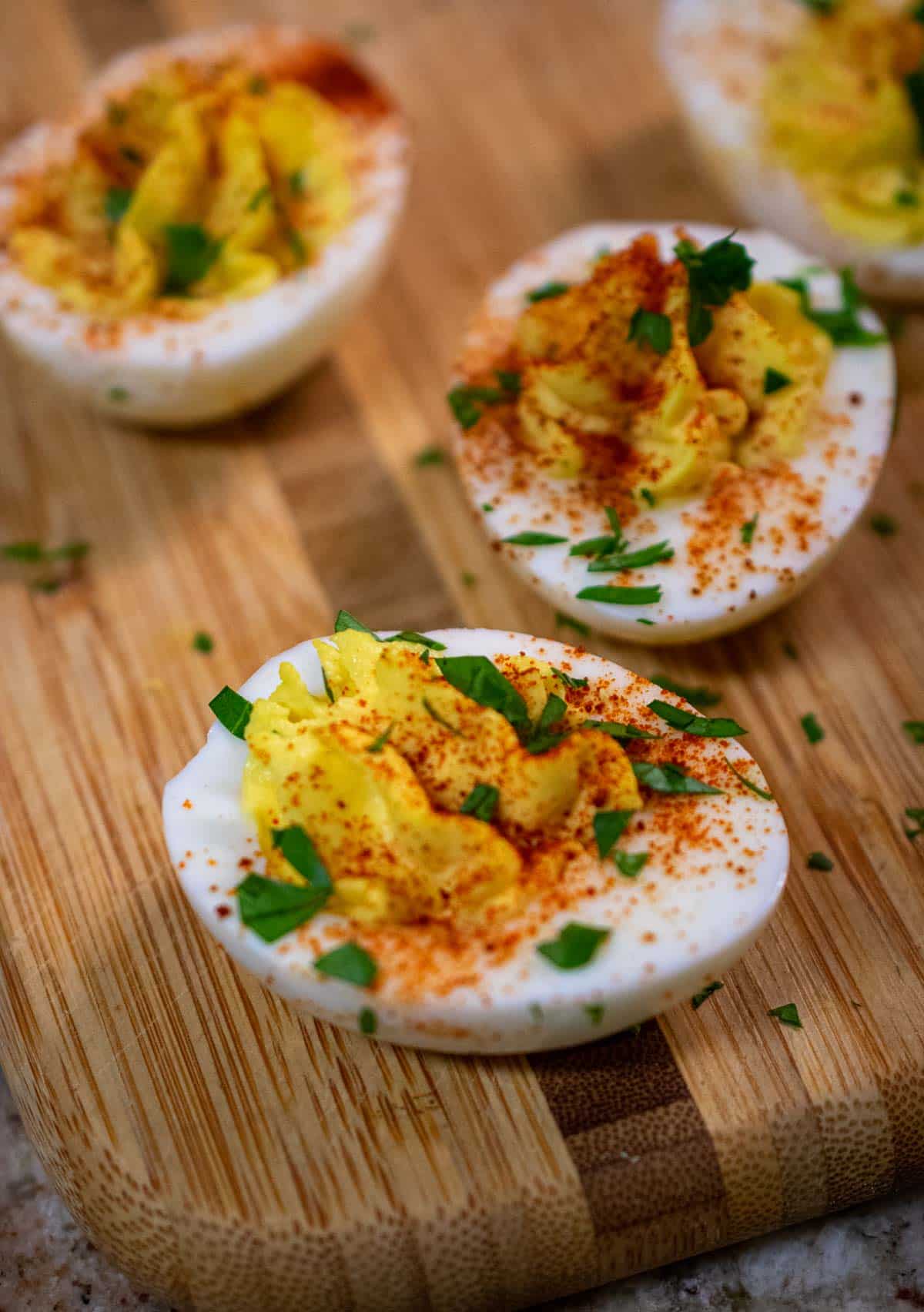 4 deviled eggs on a small wood cutting board.