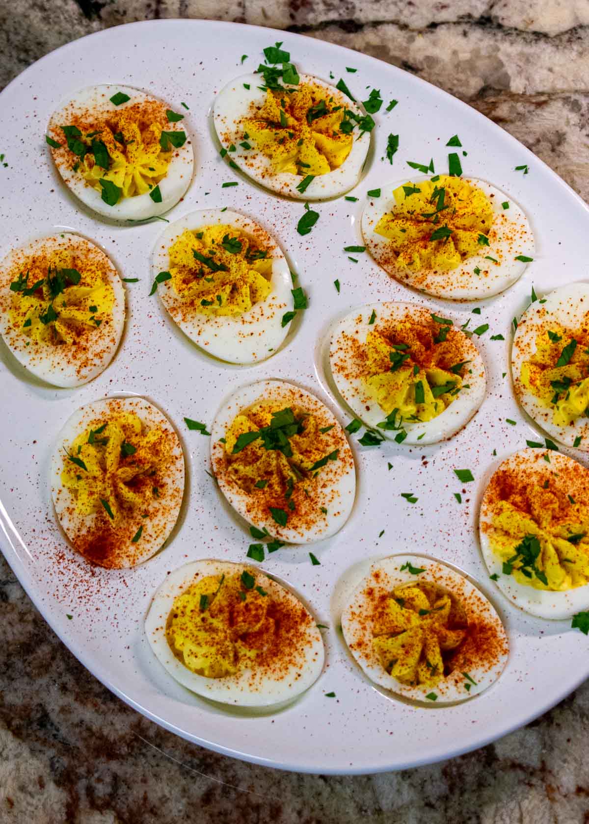 Overhead view of 12 deviled eggs sprinkled with smoked paprika and chopped parsley.