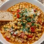 Bowl full of chickpea and pasta stew with a slice of bread.