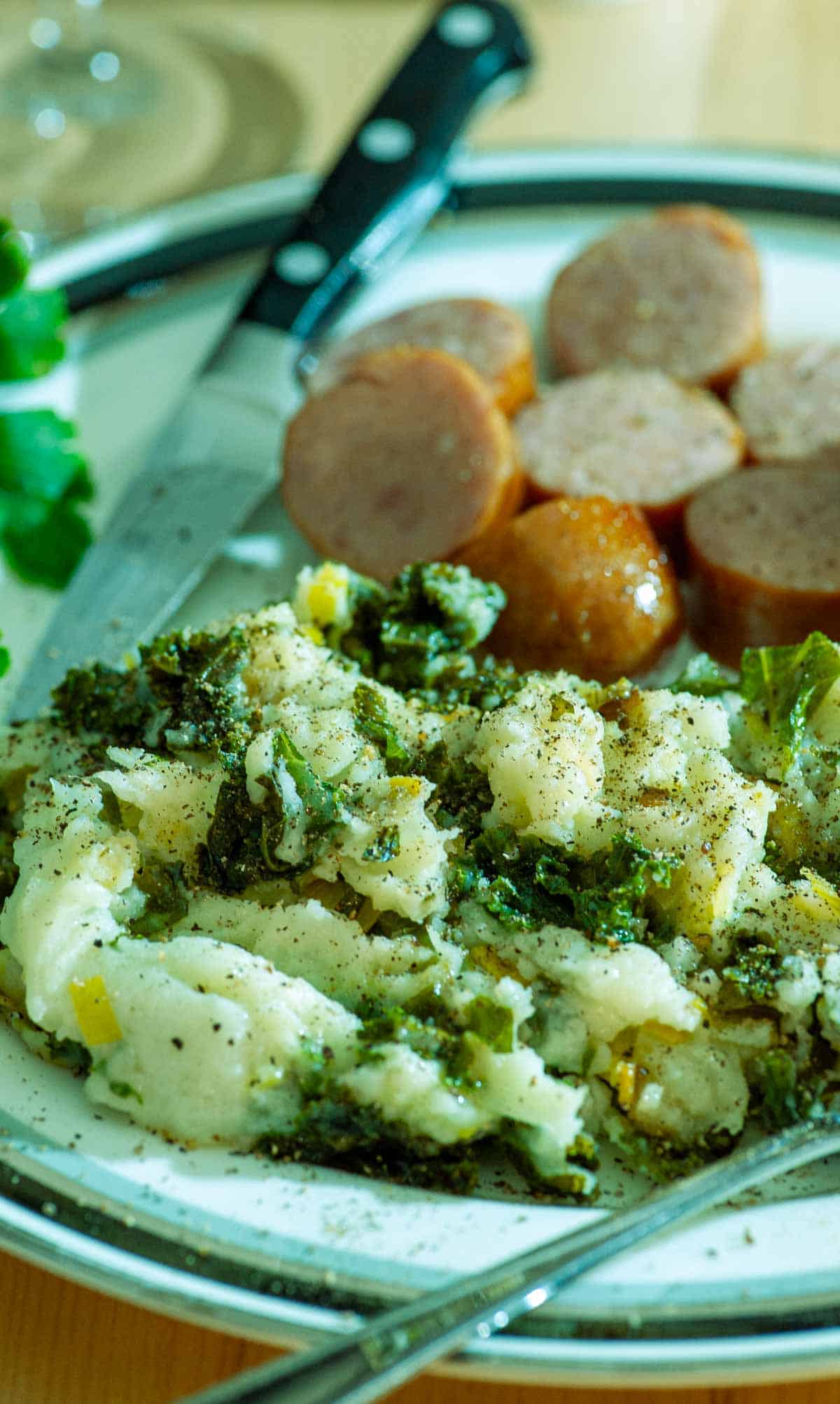 Colcannon on a plate with sausage and a knife.