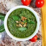 Pesto in a bowl with tomatoes and dry pasta.