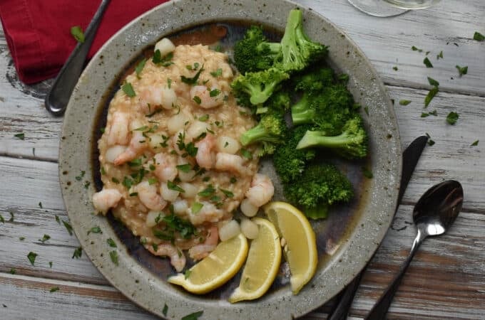 A plate of creamy seafood risotto with steamed broccoli and lemon wedges.