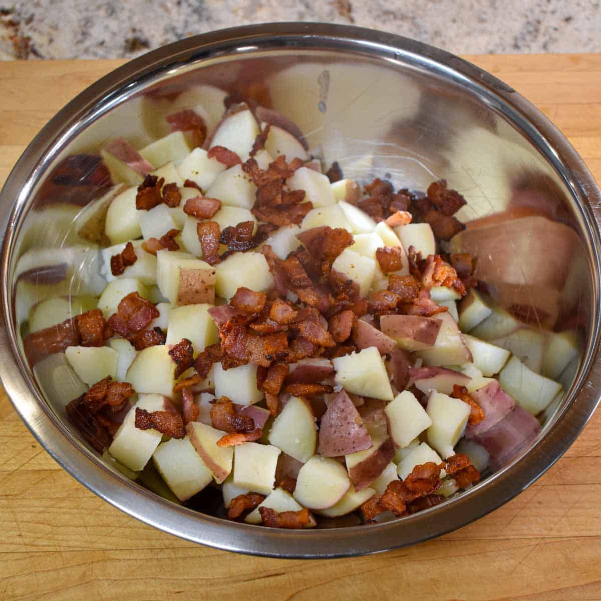 Cooed potatoes and bacon bits in a stainless steel bowl.