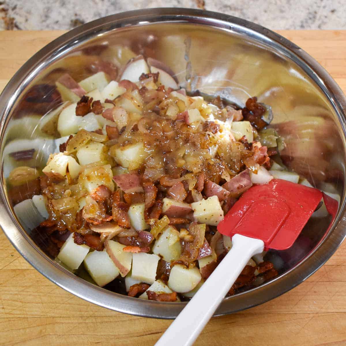 Stainless steel bowl with German potato salad ingredients ready to be stirred to coat.