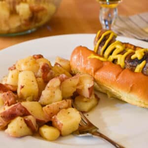 A plate of German Potato Salad with a bratwurst on a bun.
