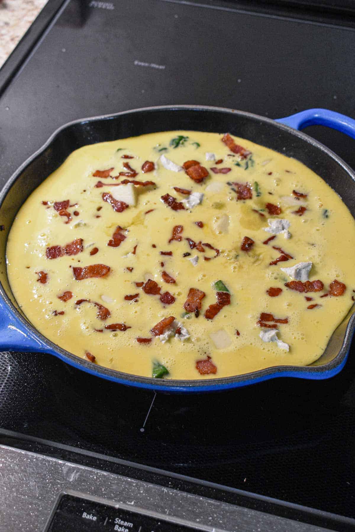 Bacon and cheese frittata on the stovetop ready to place in the oven.