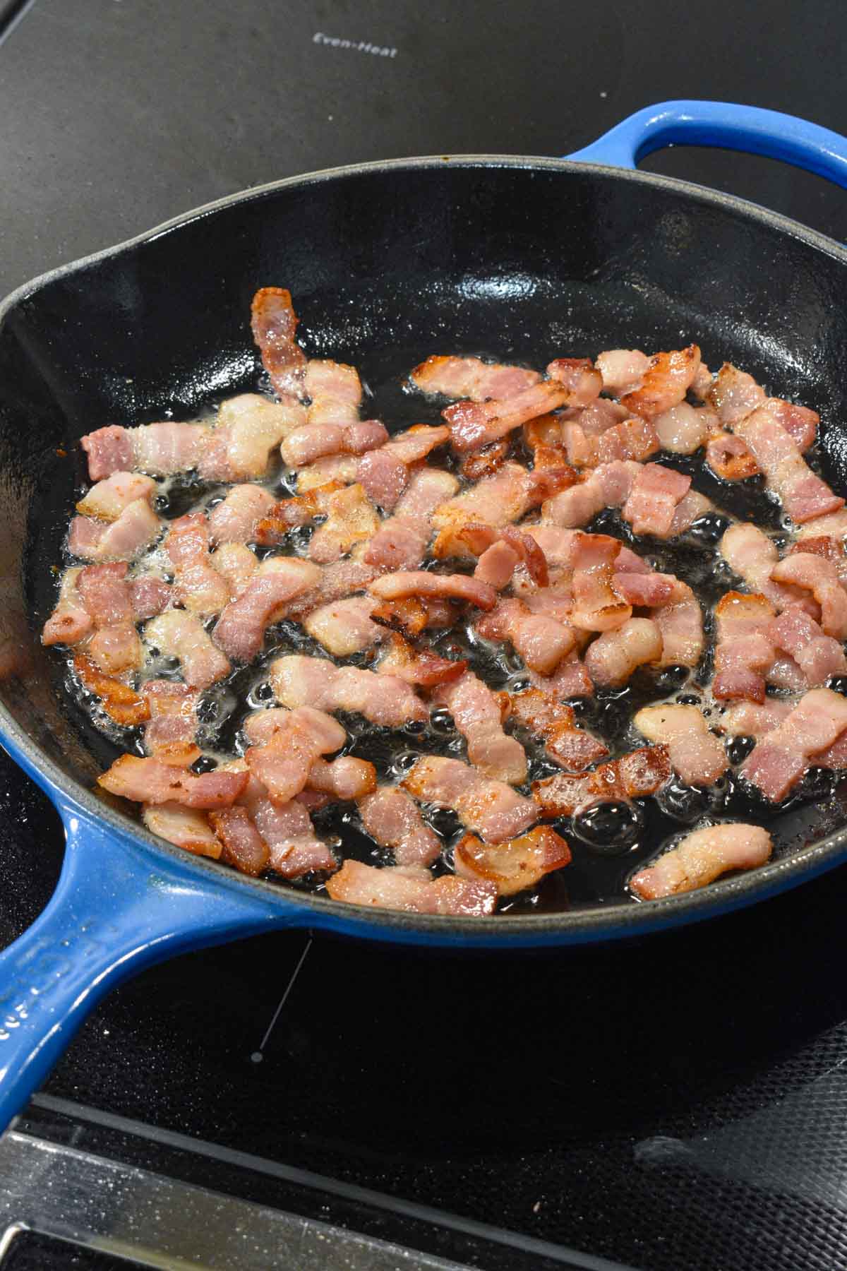 Chopped bacon frying in a cast iron skillet.