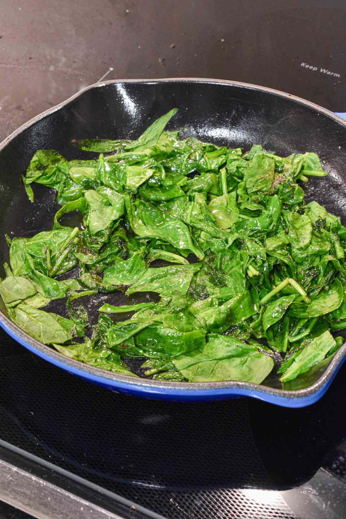 Fresh spinach being wilted in a skillet on the stovetop.